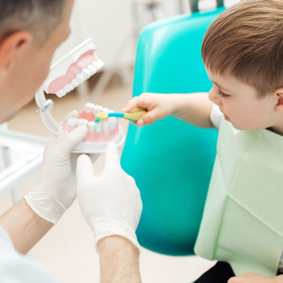 Dentist teaching little boy bruching teeth in dental clinic Dentist teaching cute little boy bruching teeth with toothbrush in dental clinic